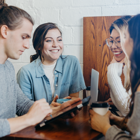 Besprechung Vier Personen sitzen gemeinsam an einem Tisch und unterhalten sich.
